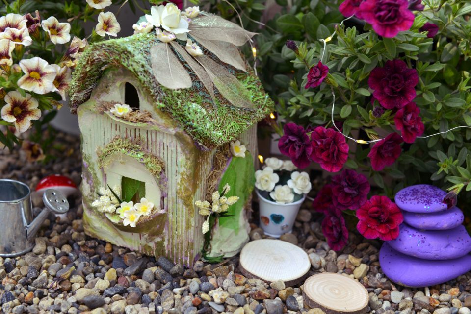 Small fairy cottage with petunia flowers outside in the garden.