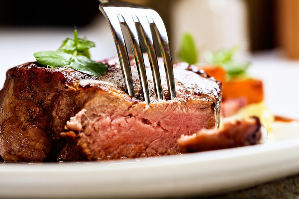 A fork pierces a juicy, grilled fillet steak, grilled medium rare.