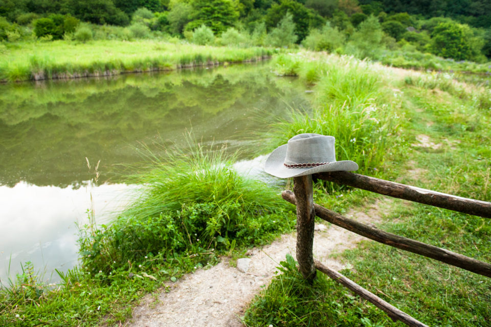 ranch with wooden fence, cowboy hat, footpath, pond and vegetation
